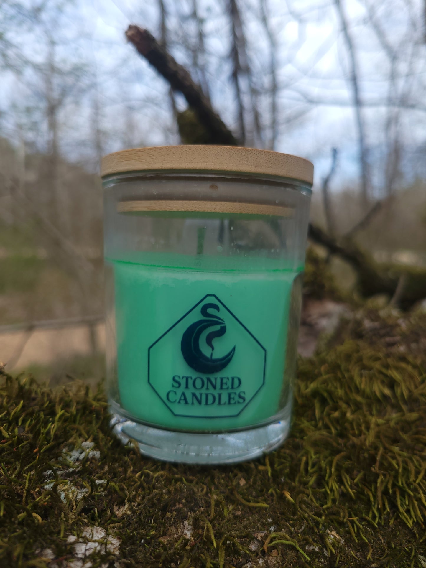 Green candle in a glass jar with a wooden lid on a mossy surface