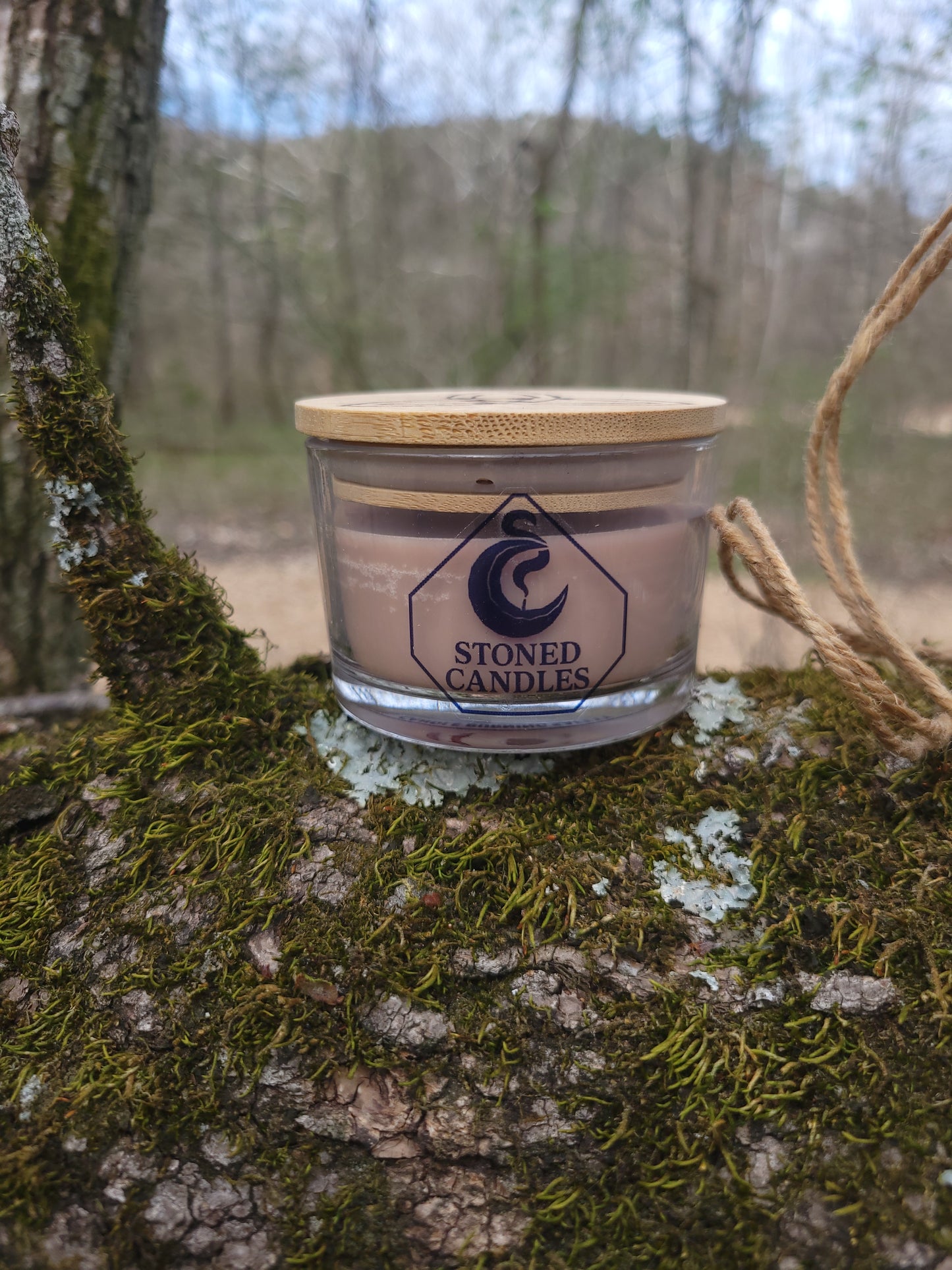 Candle in a wooden holder hanging on a tree branch with a blurred natural background