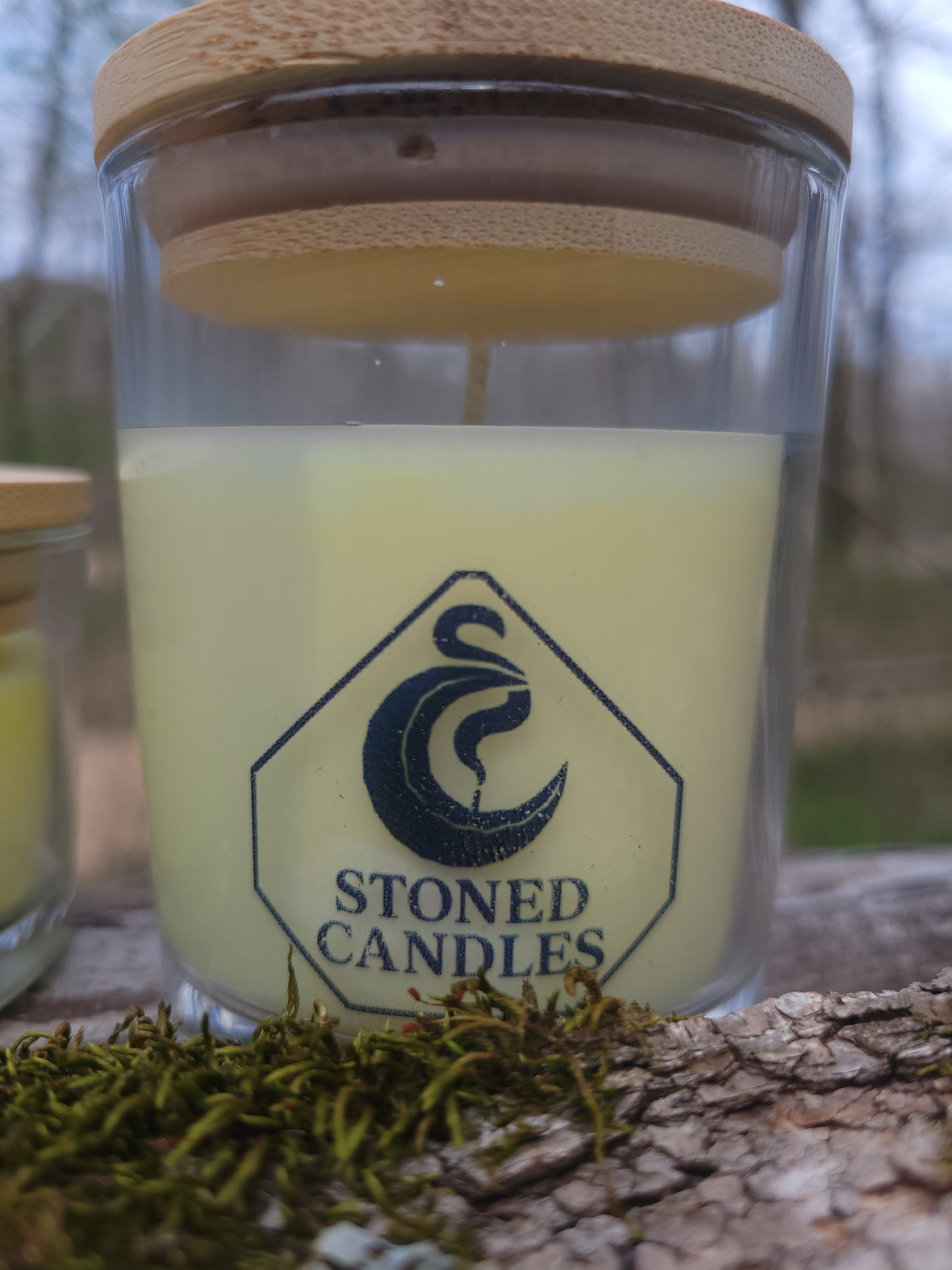 Candle in a glass jar with a wooden lid, featuring the 'Stoned Candles' logo, against a natural background.