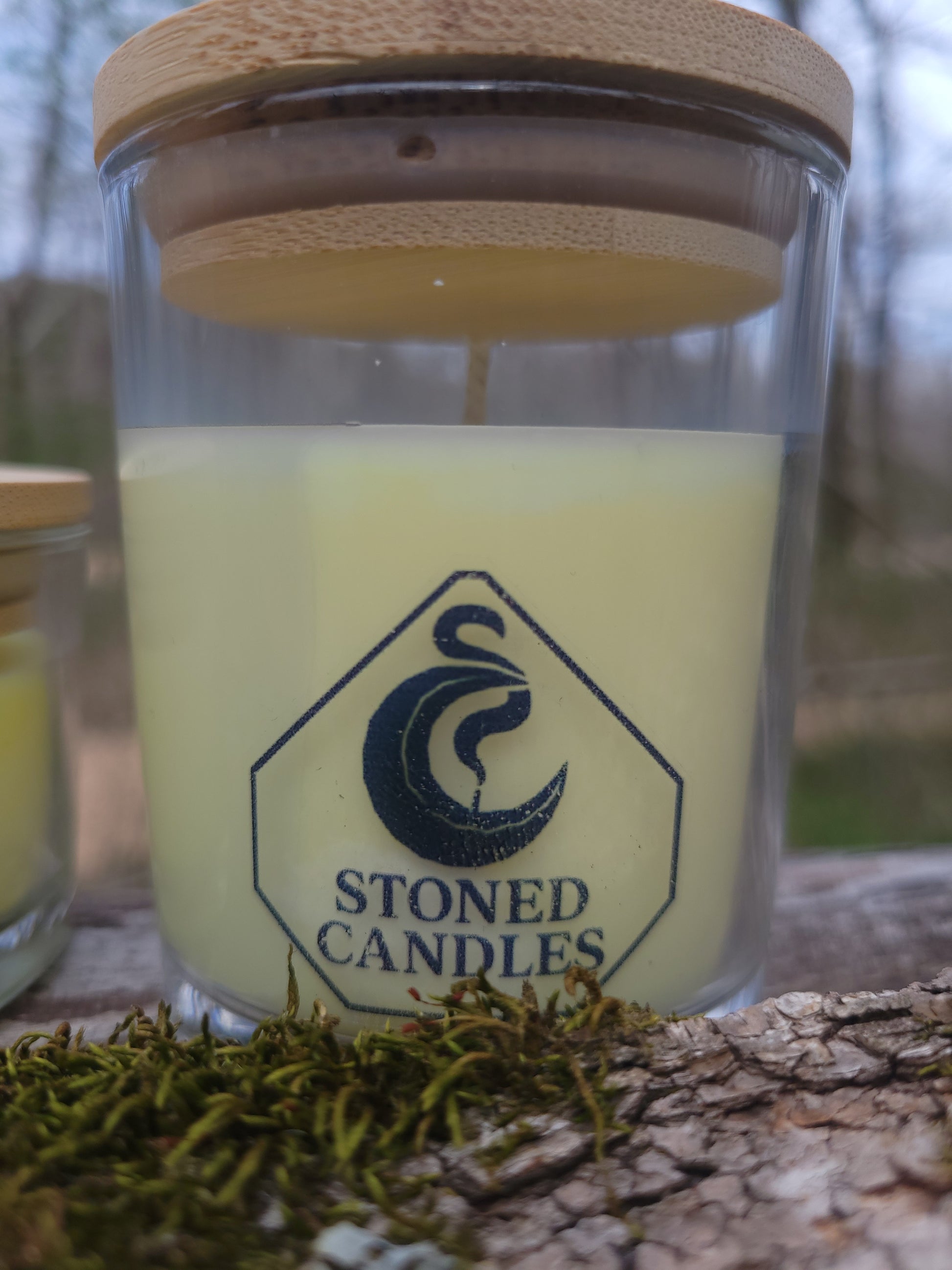 Candle in a glass jar with a wooden lid, featuring the 'Stoned Candles' logo, against a natural background.