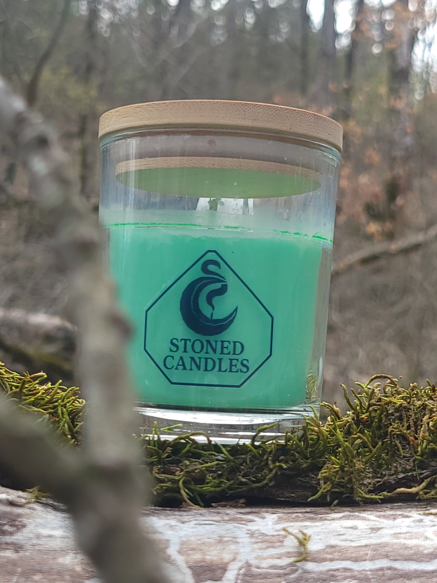 Green candle in a glass jar with 'Stoned Candles' label on a natural background