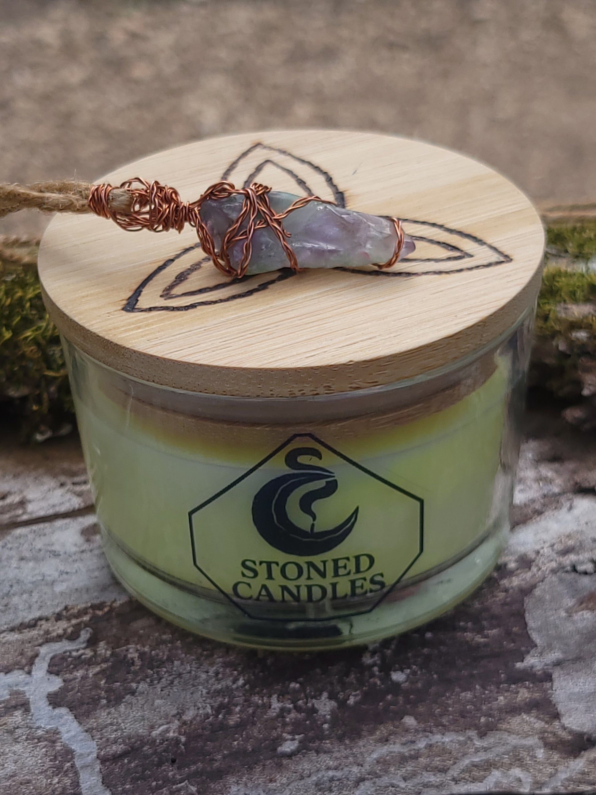 Candle with wooden lid featuring a decorative stone and 'Stoned Candles' branding.
