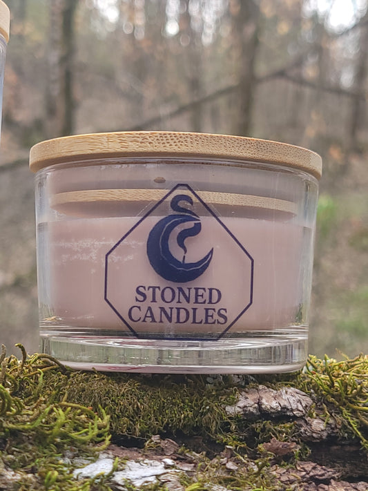 Glass candle with wooden lid on a tree branch with moss, featuring 'Stoned Candles' branding.