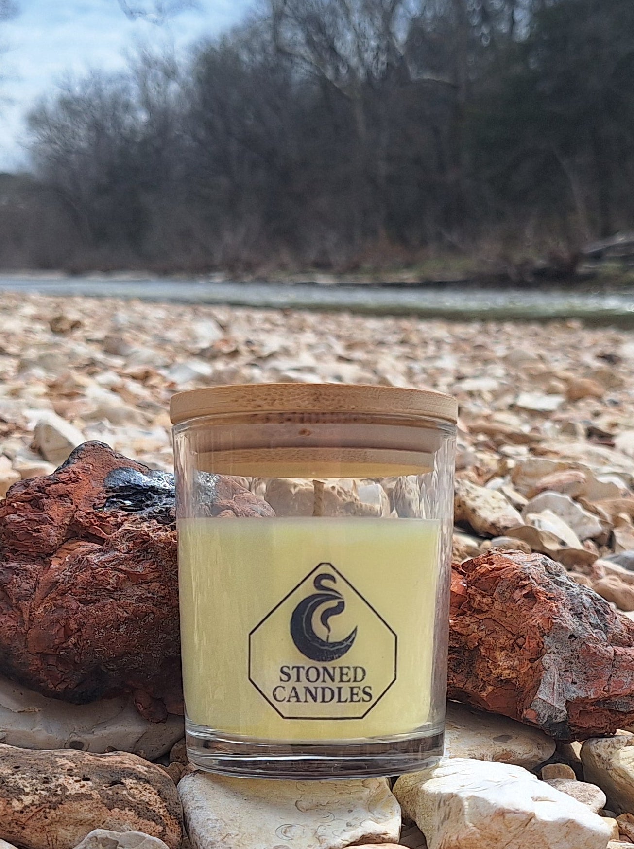 Candle in a glass jar with wooden lid on rocks near a river