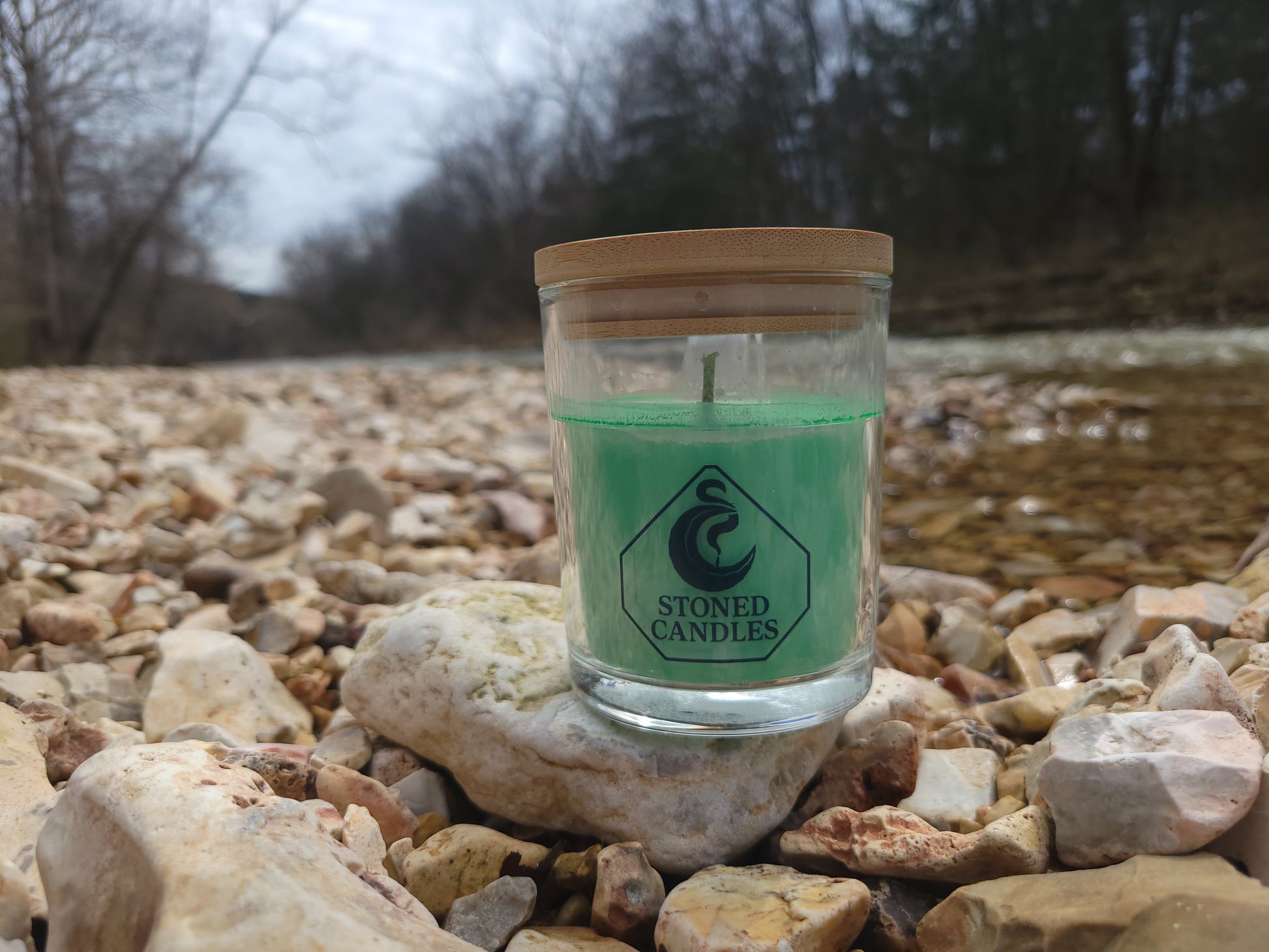 Green candle in a clear container with a brand logo on rocks