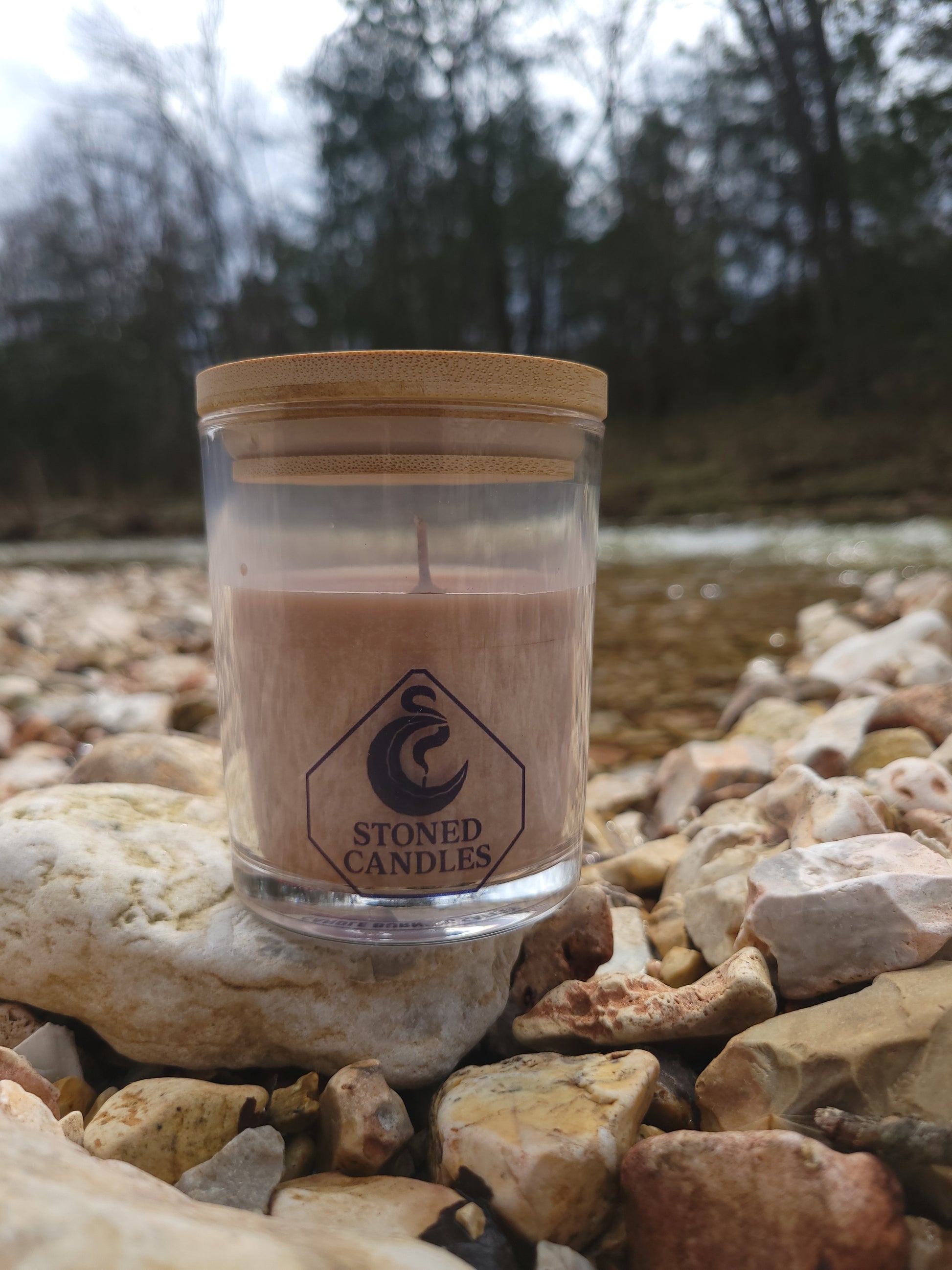 Clear glass candle jar with wooden lid on a rocky surface