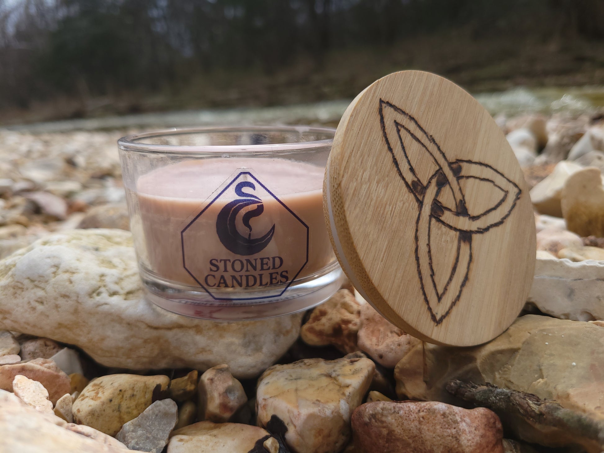 Candle with wooden lid featuring a design, placed on a stone surface.