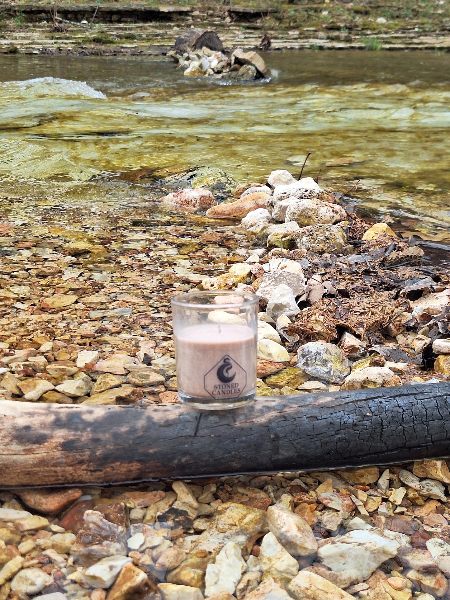Candle in a glass holder on a rocky surface with water in the background