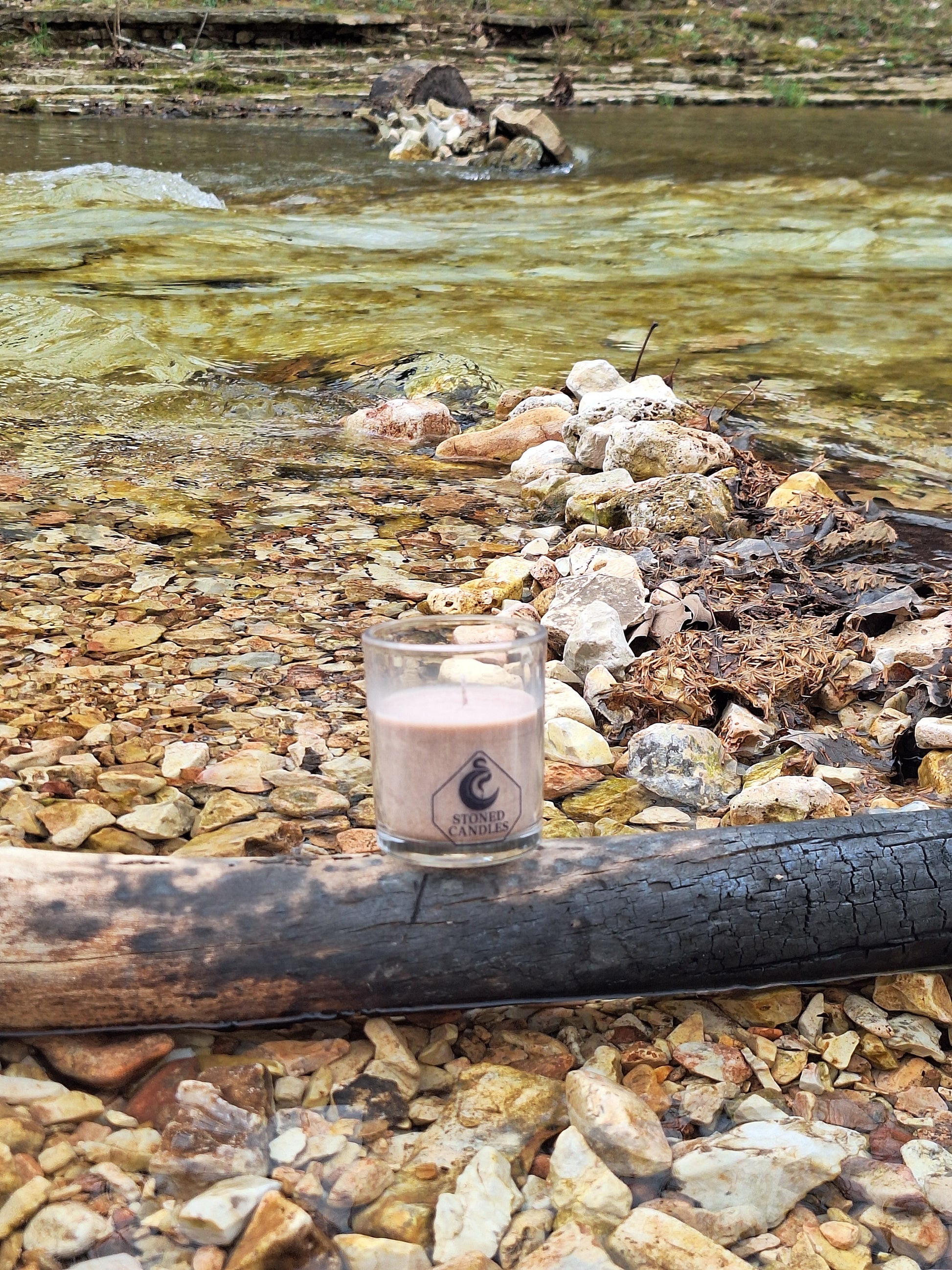 Candle in a glass holder on a rocky surface with water in the background