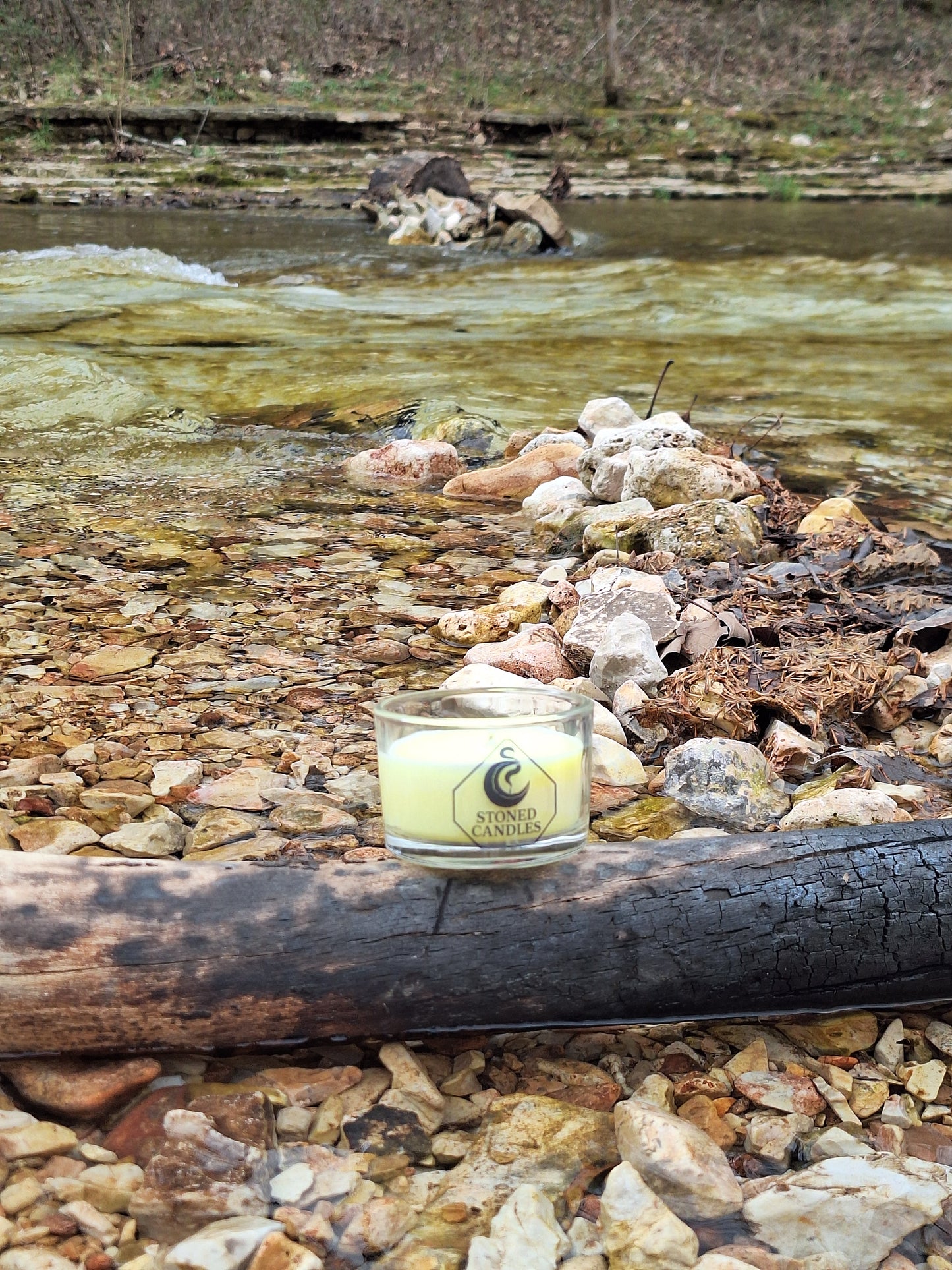 Small candle with a label on a rocky surface near water