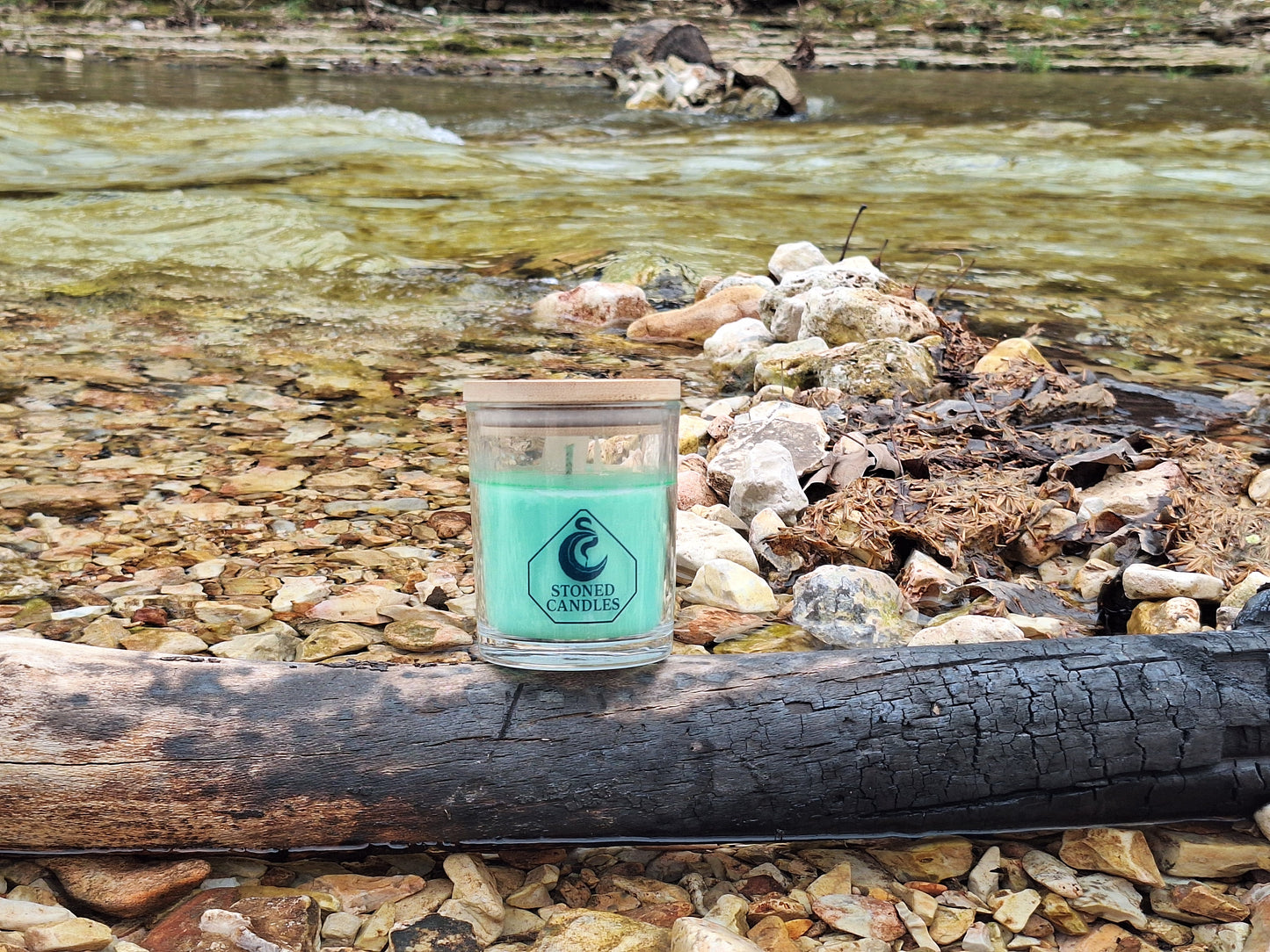 Candle in a rustic setting by a stream with rocks and logs.