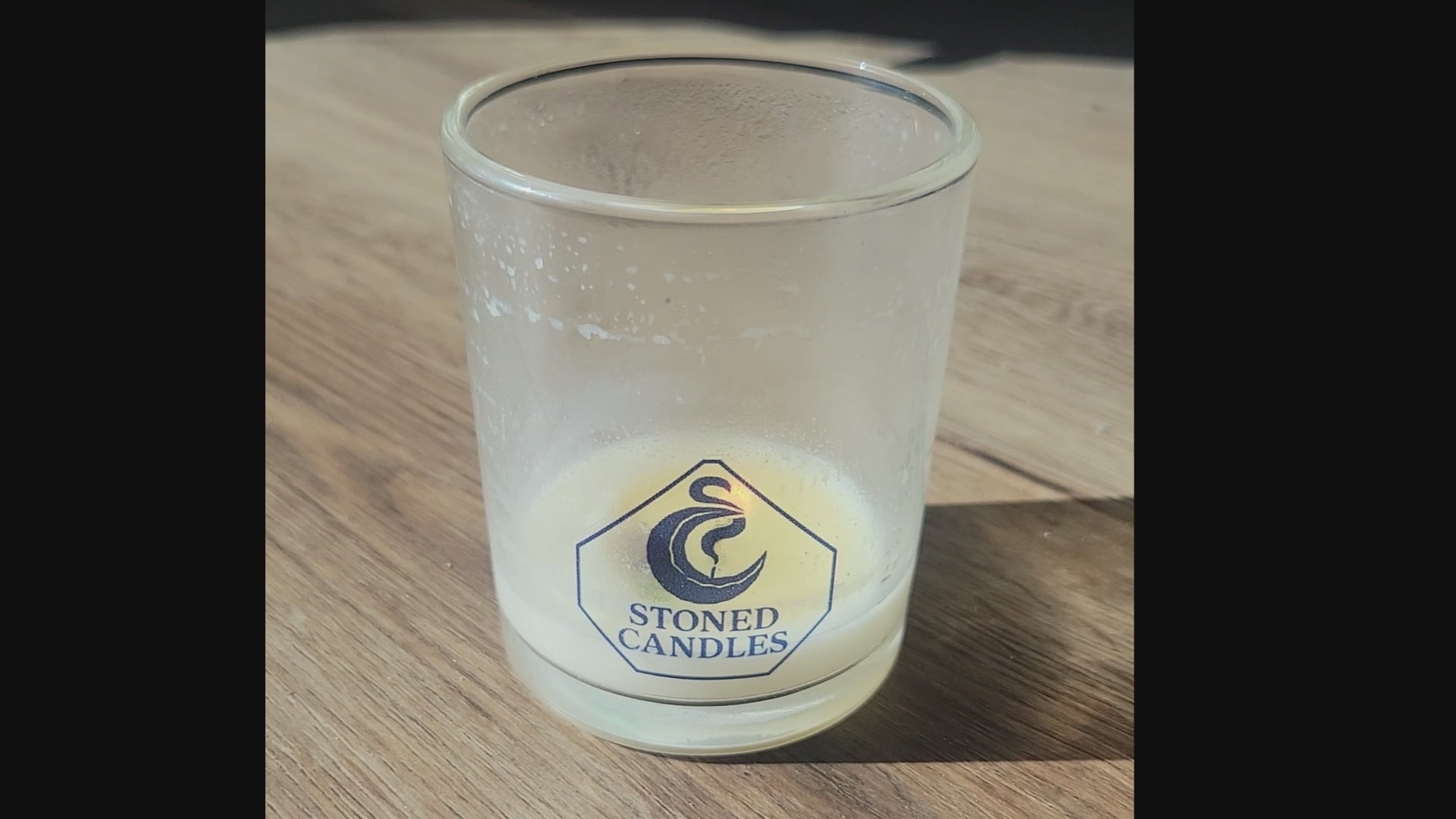 Load video: A panning up and down video of a candle burning very low and as the video looks directly down at the burning wick, a gemstone is clearly visible in the melted wax. Panning back down, one sees the Stoned Candles Logo with the flame directly behind it.